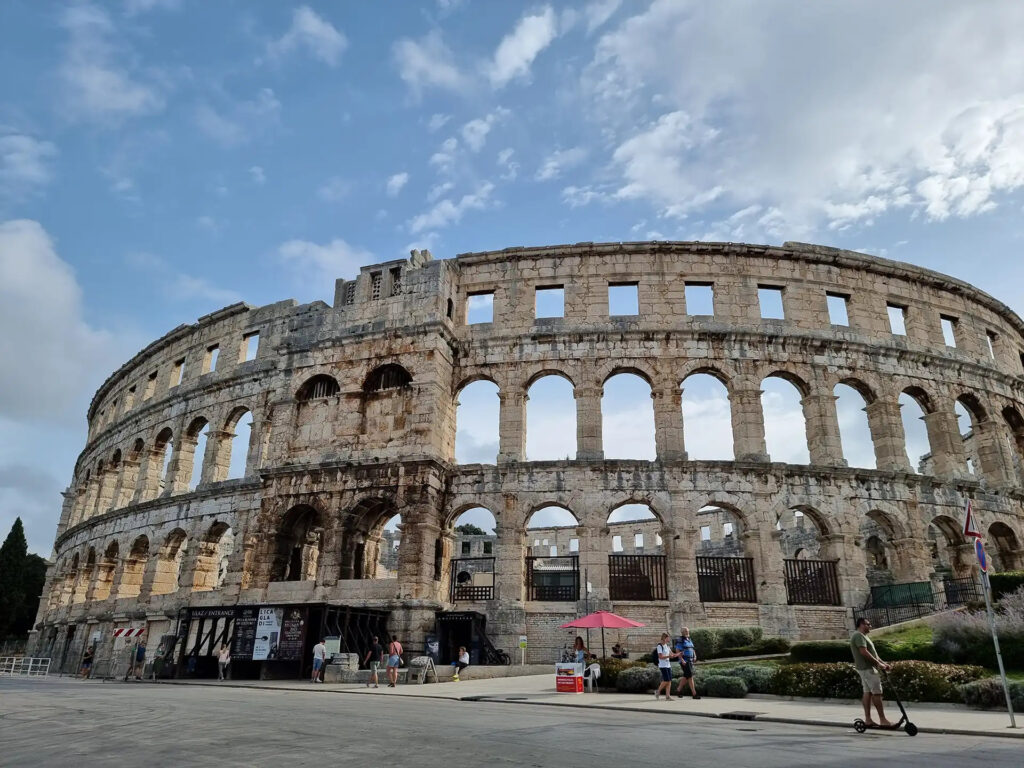 Exterior view of the Pula Amphitheatre’s stone facade against the sky.