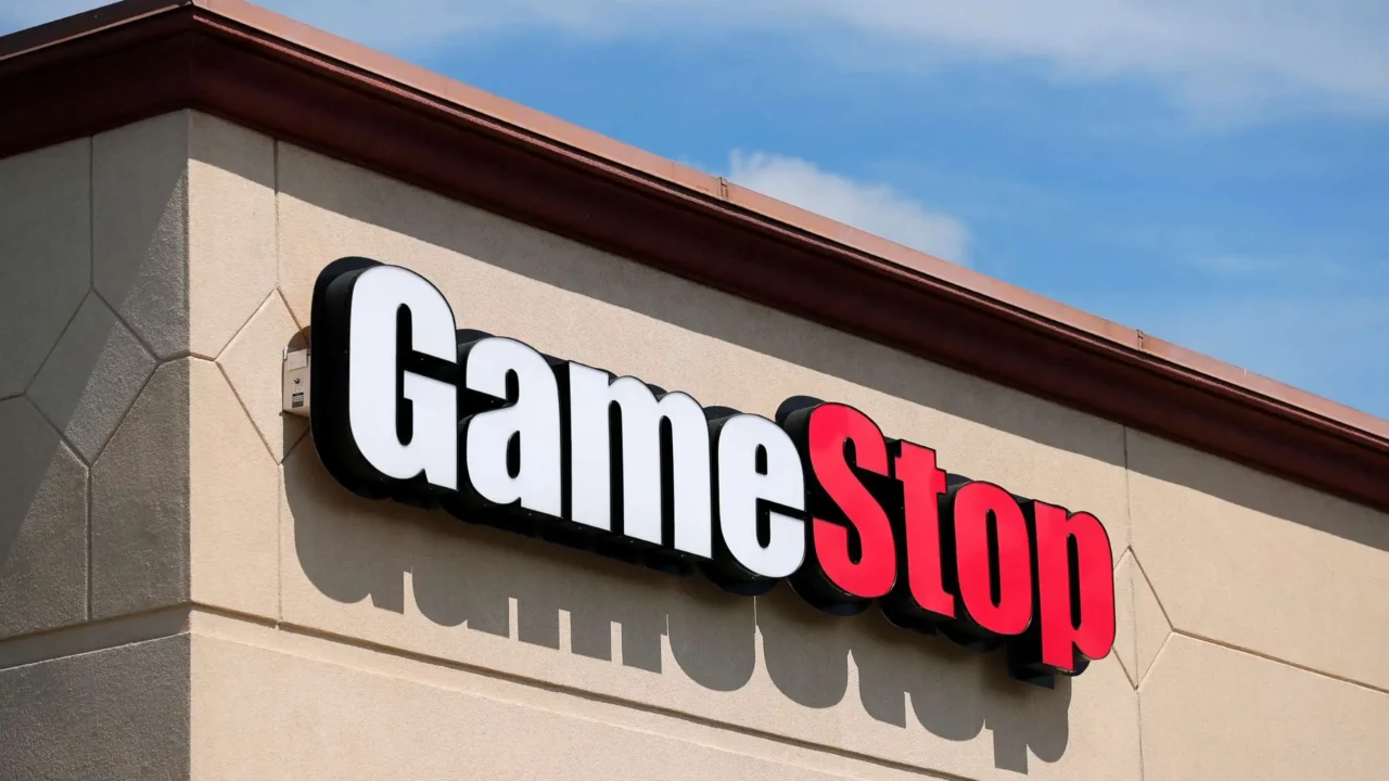 The GameStop logo on the side of a retail store under a blue sky