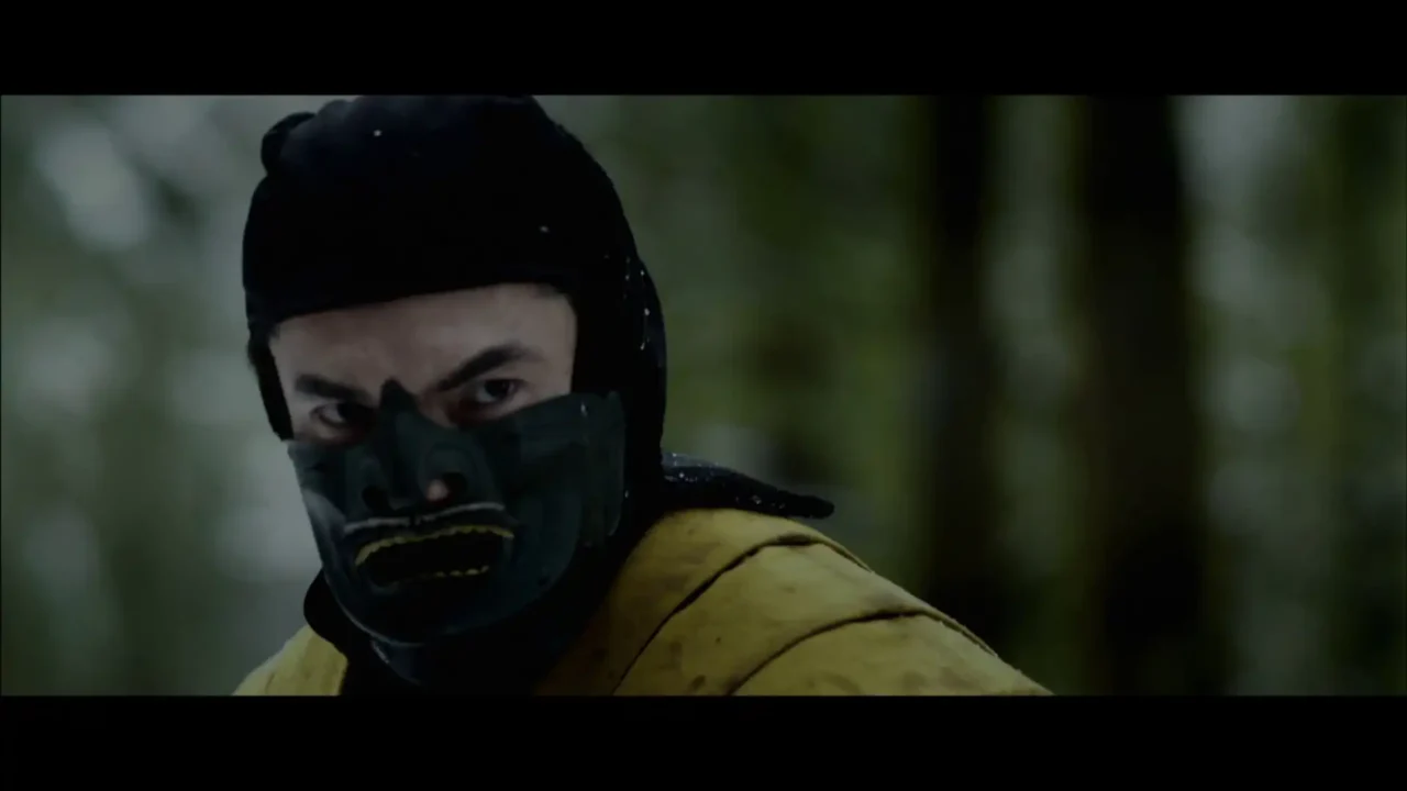 Masked fighter in yellow gear staring forward in a forest setting.