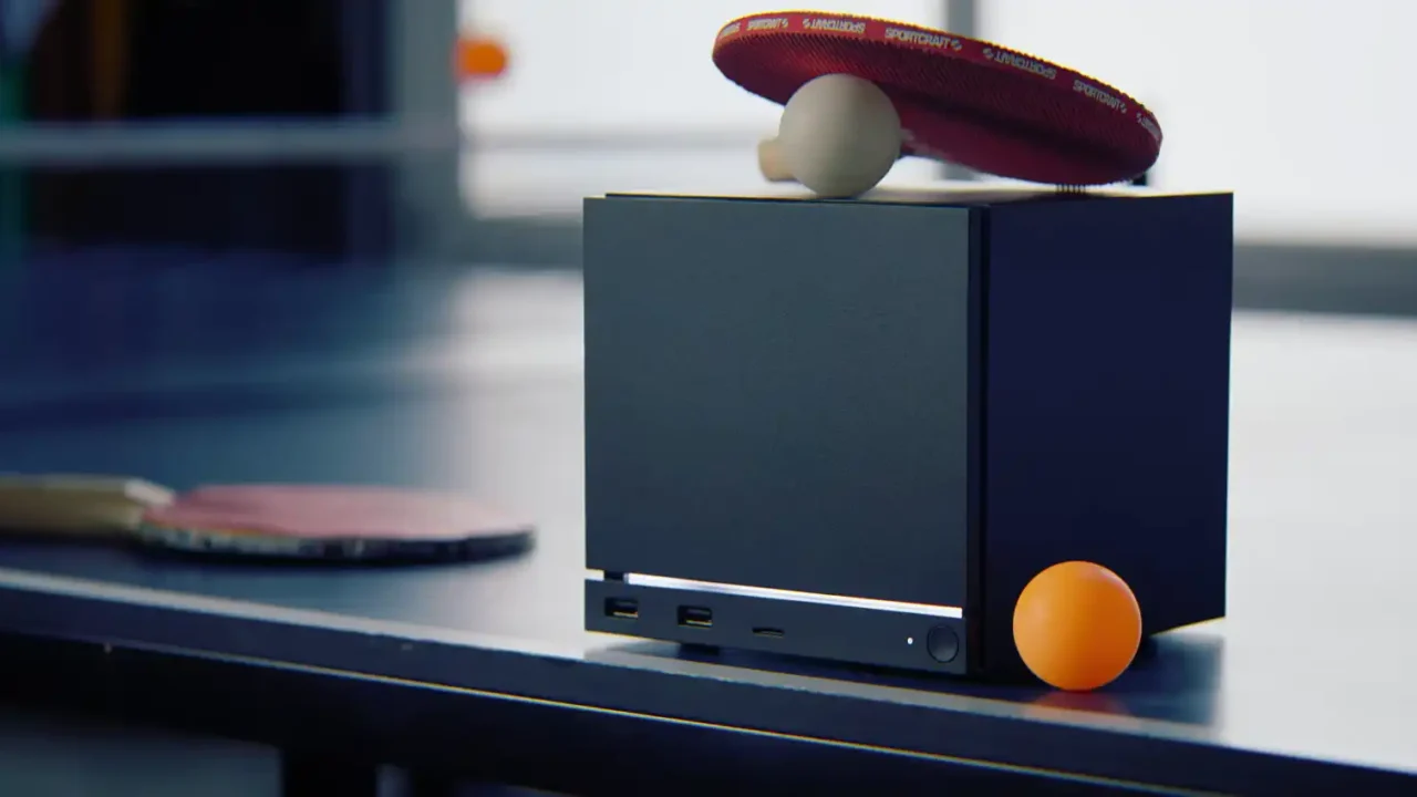 Steam Machine-style mini PC sitting on a table tennis table with a paddle and ball nearby.