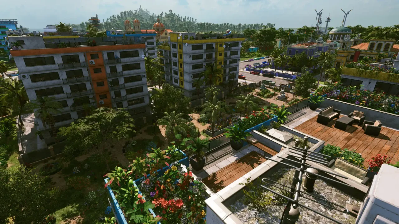 Tropico 7 gameplay screenshot showing apartment blocks, rooftop terraces, and landscaped gardens in a tropical district