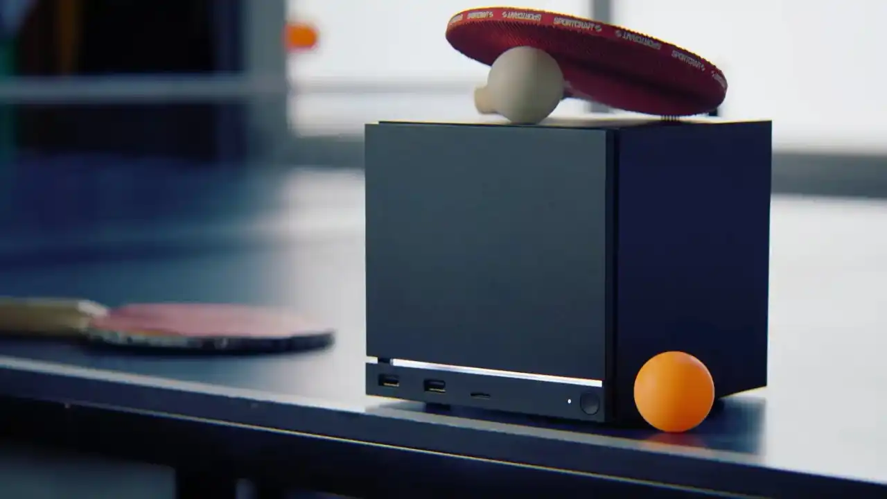 Compact Steam Machine-style mini PC on a desk with a monitor in the background