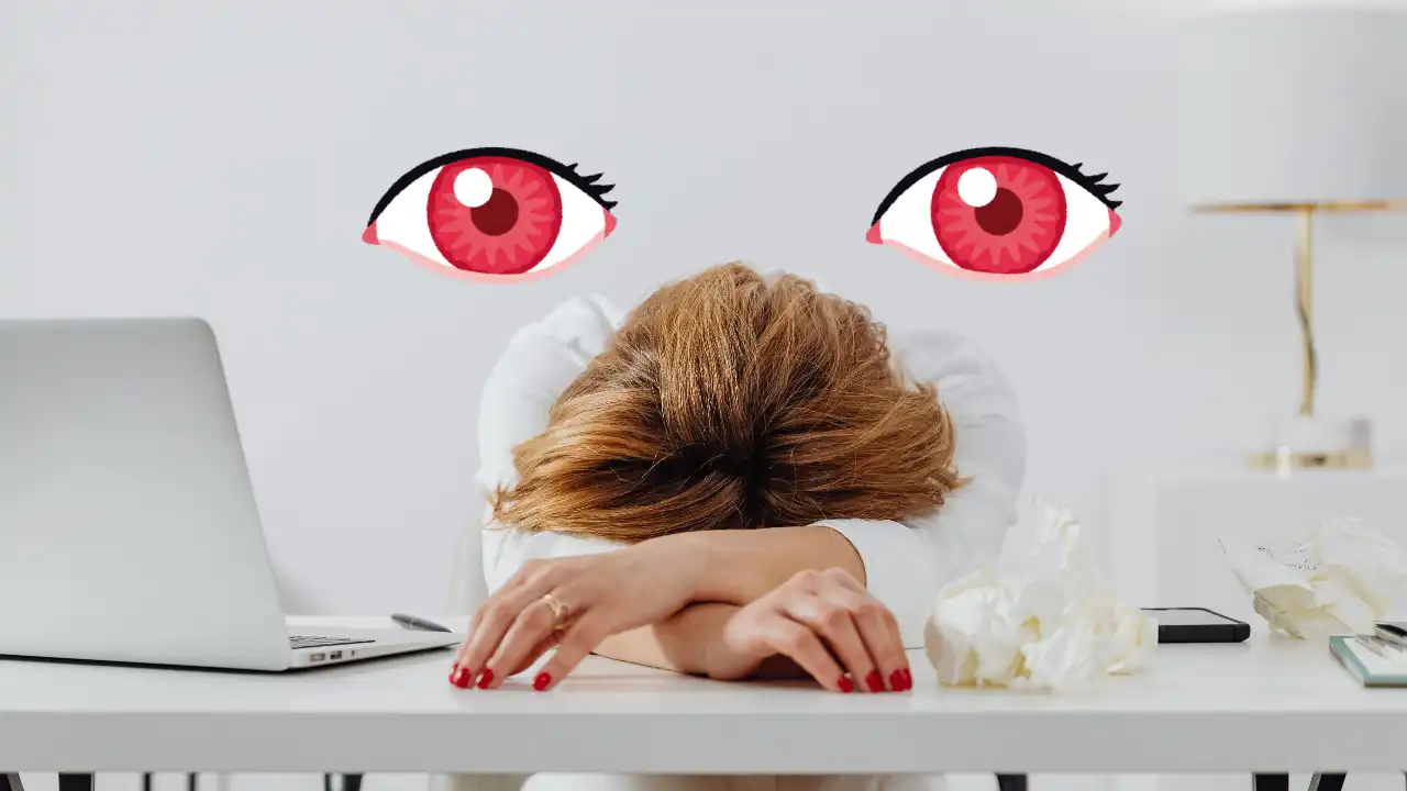 Person resting their head on a desk beside a laptop with illustrated red tired eyes above