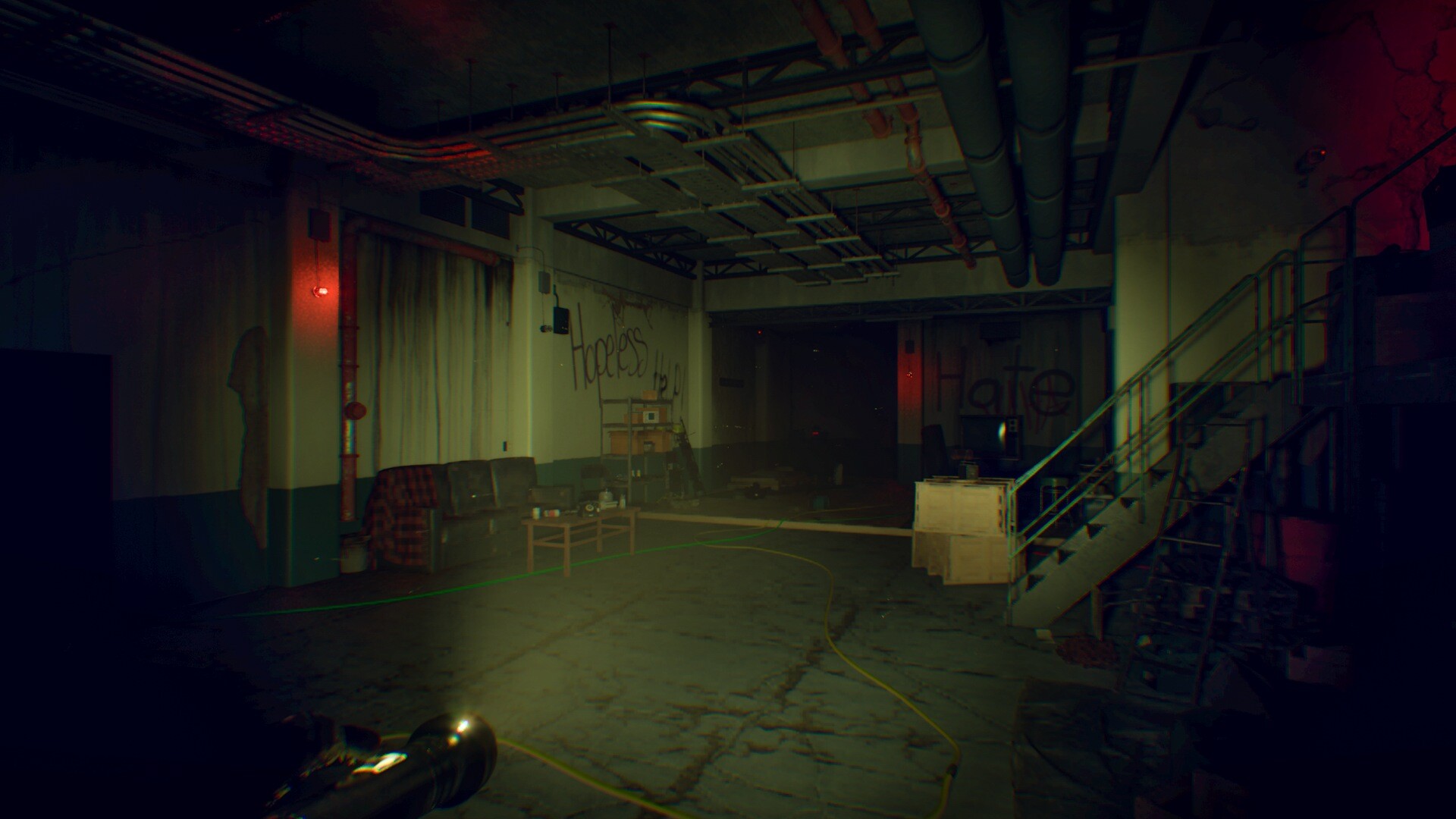 Dark garage-like bunker interior in Pestilence, with overhead pipes, scattered cables, a metal stairway and red lights.