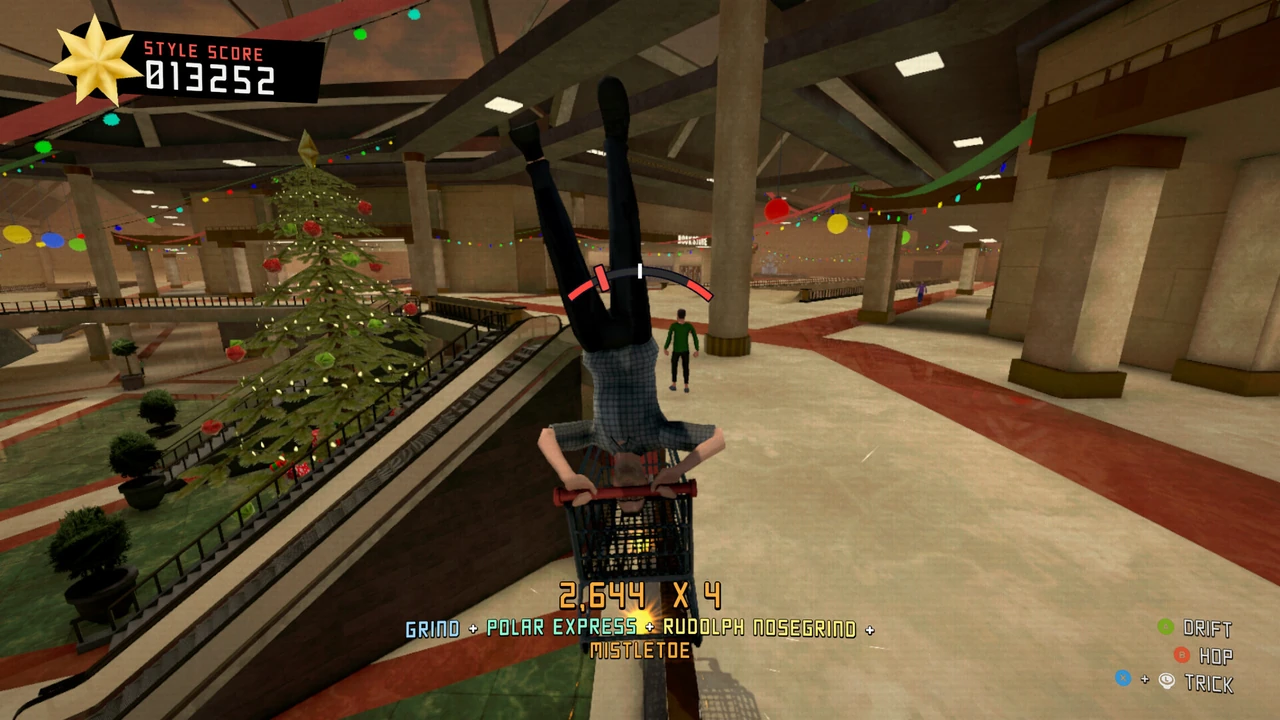 A Yule Dads character balancing upside down in a shopping cart beside a Christmas tree inside a decorated shopping mall.
